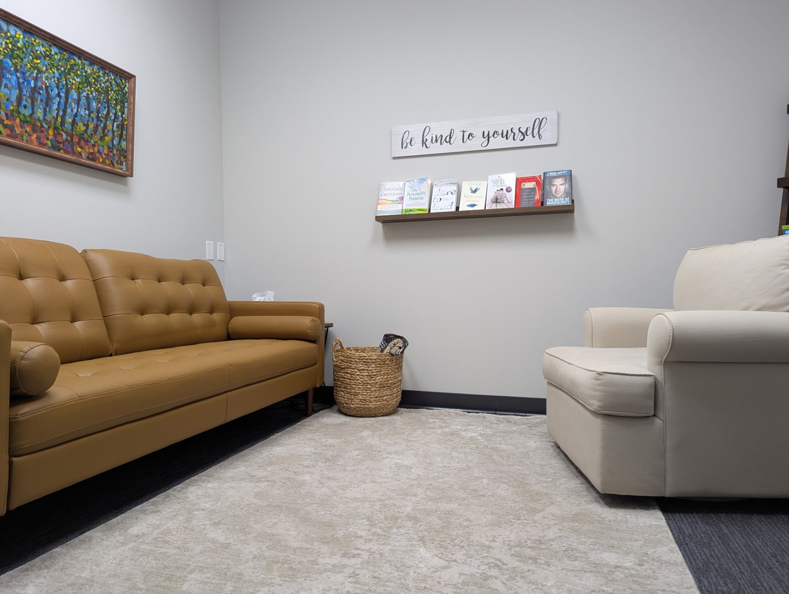 Calgary counselling room with a warm leather couch, bookshelf and a 'be kind to yourself' sign